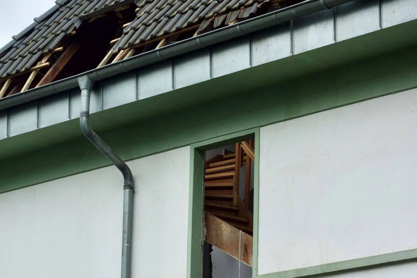 Storm-torn roof with missing tiles and exposed wooden structure after severe weather